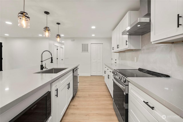 kitchen with light wood finished floors, white cabinets, stainless steel appliances, wall chimney range hood, and a sink