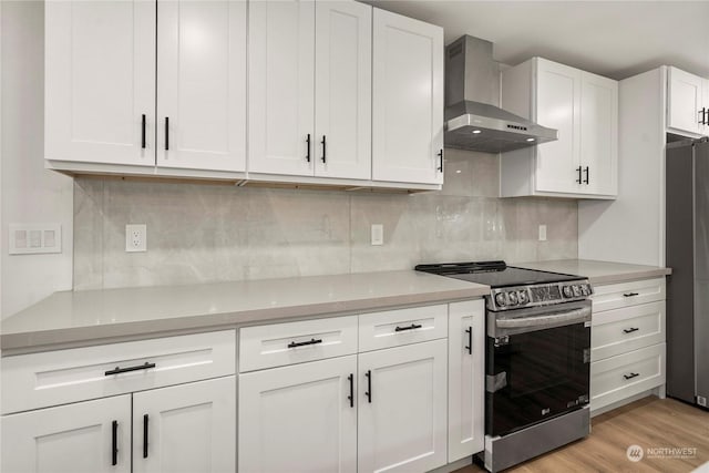 kitchen with stainless steel appliances, wall chimney range hood, light countertops, and white cabinetry