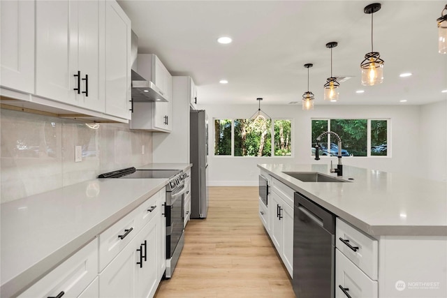 kitchen with stainless steel appliances, a sink, light countertops, wall chimney range hood, and tasteful backsplash