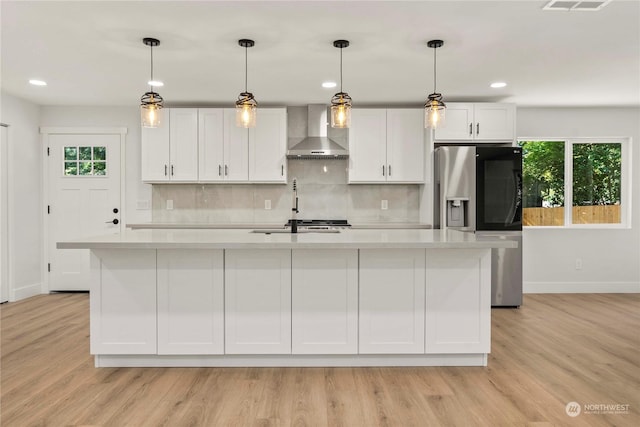 kitchen with an island with sink, wall chimney range hood, light countertops, and stainless steel fridge with ice dispenser