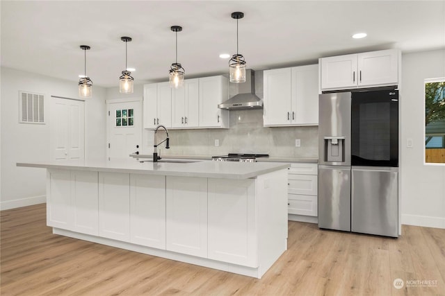 kitchen with stainless steel fridge, visible vents, light countertops, wall chimney range hood, and a sink