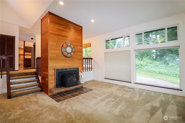 carpeted living room featuring a wood stove, high vaulted ceiling, and a tile fireplace