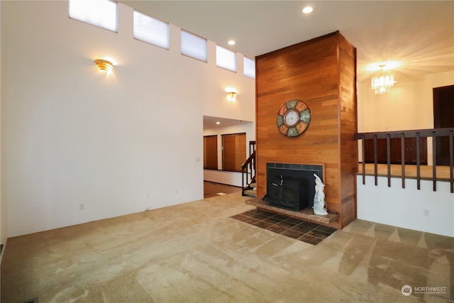 carpeted living room with a tile fireplace, wooden walls, an inviting chandelier, a wood stove, and a towering ceiling