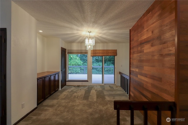 unfurnished living room featuring a textured ceiling, an inviting chandelier, and light carpet