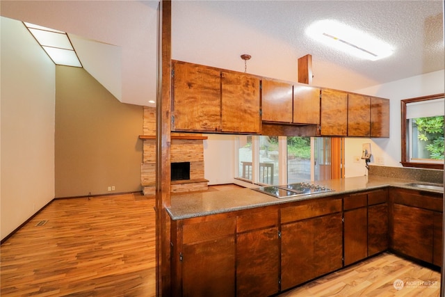 kitchen featuring light hardwood / wood-style flooring, electric cooktop, lofted ceiling, a stone fireplace, and a textured ceiling