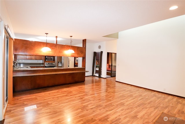 kitchen with hardwood / wood-style floors, appliances with stainless steel finishes, sink, kitchen peninsula, and pendant lighting