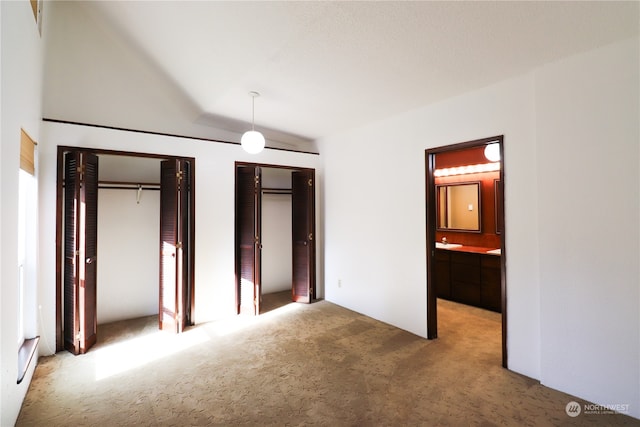 unfurnished bedroom featuring lofted ceiling, ensuite bathroom, two closets, and carpet flooring