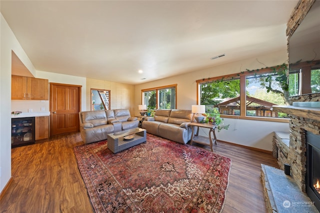 living room with dark hardwood / wood-style floors, wine cooler, and a stone fireplace