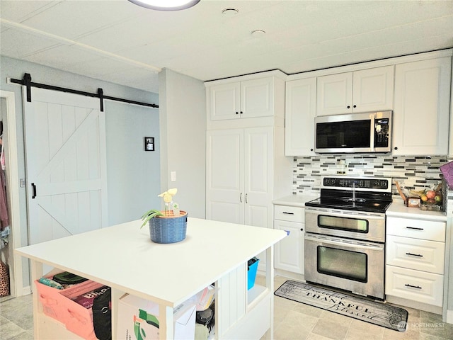 kitchen with tasteful backsplash, a barn door, white cabinets, appliances with stainless steel finishes, and light countertops