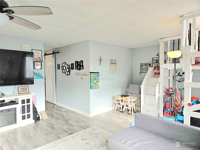 playroom featuring wood finished floors, ceiling fan, baseboards, and a barn door