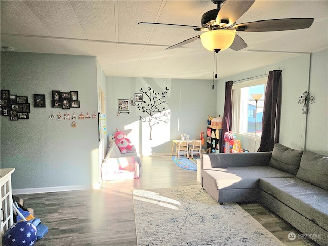 living room with ceiling fan, baseboards, and wood finished floors