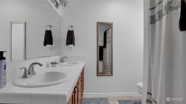 bathroom featuring double vanity, toilet, baseboards, and a sink