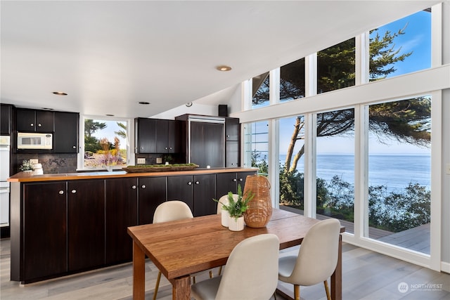 dining space with lofted ceiling, a water view, and light hardwood / wood-style flooring