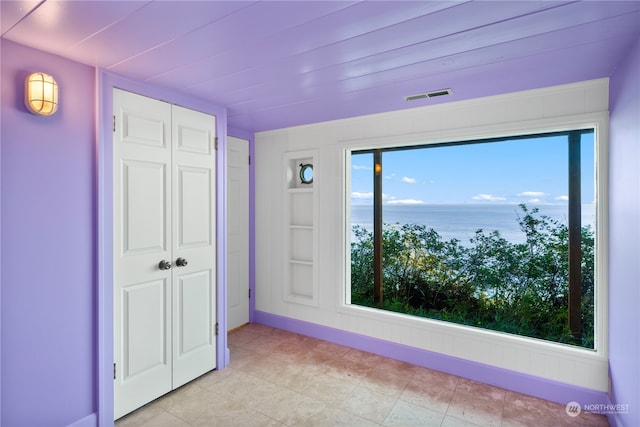 unfurnished bedroom featuring a water view, a closet, and light tile patterned floors