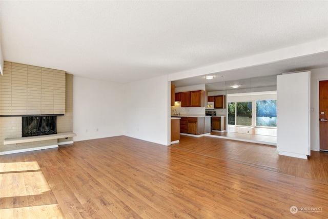 unfurnished living room with light wood-type flooring, sink, a textured ceiling, and a brick fireplace