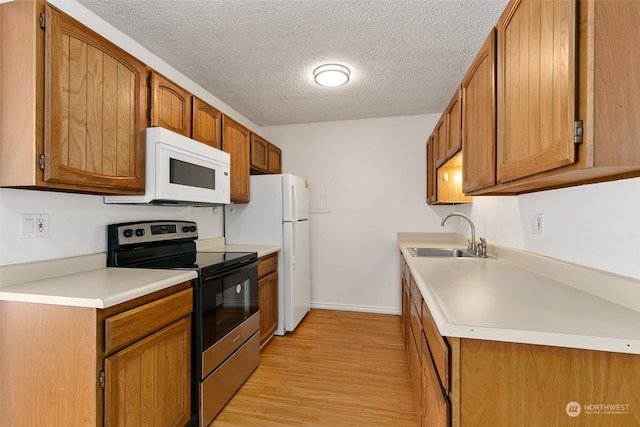 kitchen featuring a textured ceiling, sink, white appliances, and light hardwood / wood-style floors