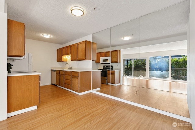 kitchen with stainless steel appliances, sink, a textured ceiling, and light hardwood / wood-style flooring