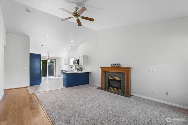 unfurnished living room featuring light wood-style flooring, a tiled fireplace, a sink, vaulted ceiling, and ceiling fan