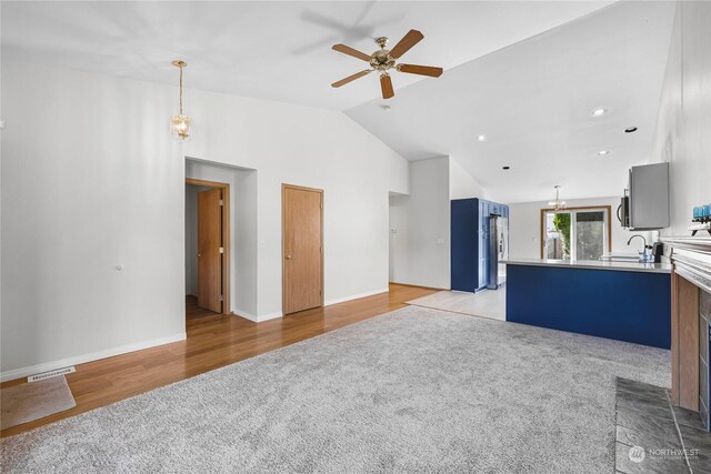 unfurnished living room featuring visible vents, light colored carpet, light wood-type flooring, a sink, and ceiling fan with notable chandelier