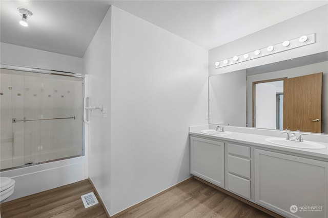 full bathroom featuring vanity, toilet, wood-type flooring, and bath / shower combo with glass door