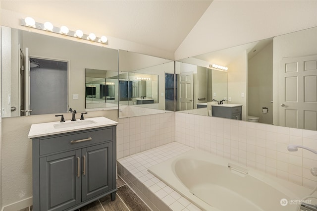 bathroom featuring vanity, lofted ceiling, toilet, and a relaxing tiled tub