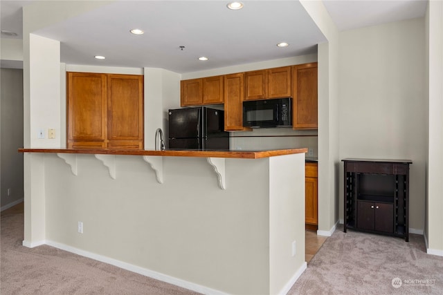 kitchen featuring light carpet, sink, black appliances, kitchen peninsula, and a breakfast bar