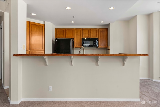 kitchen featuring black appliances, a kitchen breakfast bar, and light carpet