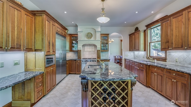 kitchen with decorative light fixtures, built in refrigerator, an island with sink, sink, and decorative backsplash