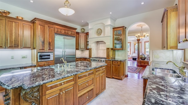 kitchen featuring a notable chandelier, sink, built in appliances, a center island with sink, and tasteful backsplash