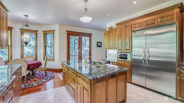 kitchen featuring built in appliances, light hardwood / wood-style floors, hanging light fixtures, and a center island with sink