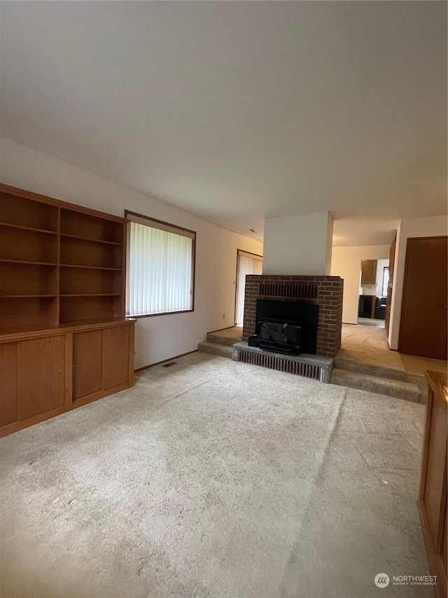 unfurnished living room featuring light carpet and a brick fireplace