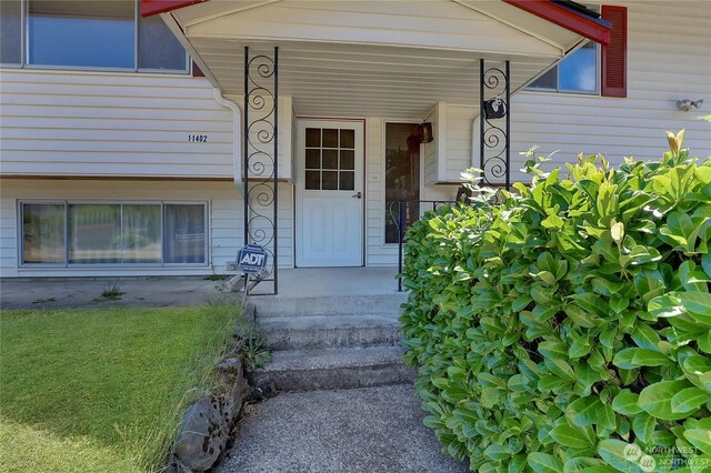 view of exterior entry featuring a yard and a porch