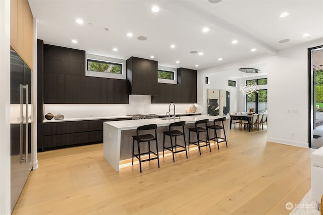 kitchen featuring light hardwood / wood-style floors, sink, wall chimney range hood, a center island with sink, and a breakfast bar