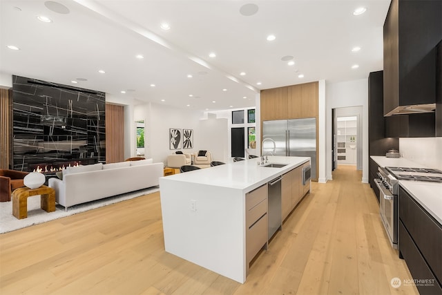 kitchen featuring a center island with sink, built in appliances, sink, and light hardwood / wood-style floors