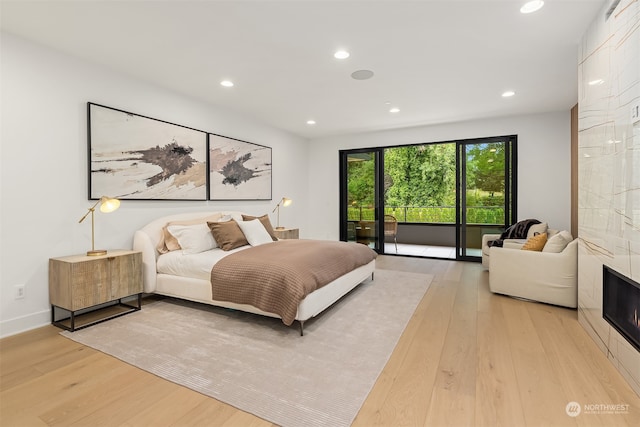 bedroom with light wood-type flooring, access to exterior, and a tile fireplace