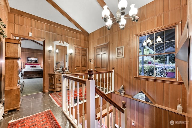 hallway with lofted ceiling, wood walls, and an inviting chandelier