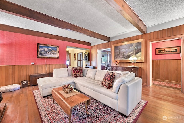 living room featuring a textured ceiling, wood walls, beamed ceiling, and hardwood / wood-style flooring