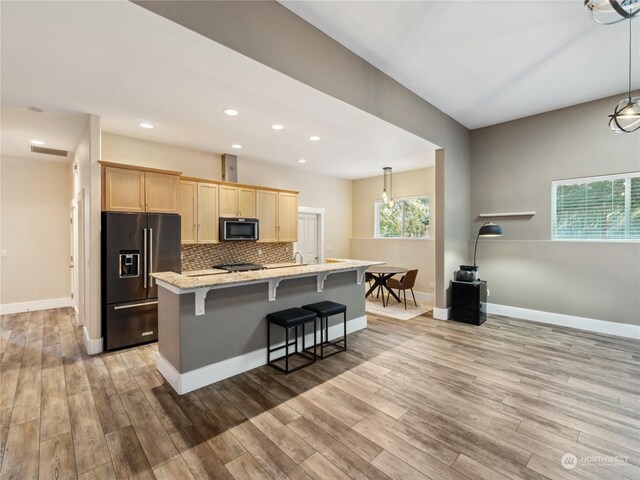 kitchen featuring a kitchen island with sink, high end fridge, light hardwood / wood-style floors, and light brown cabinets