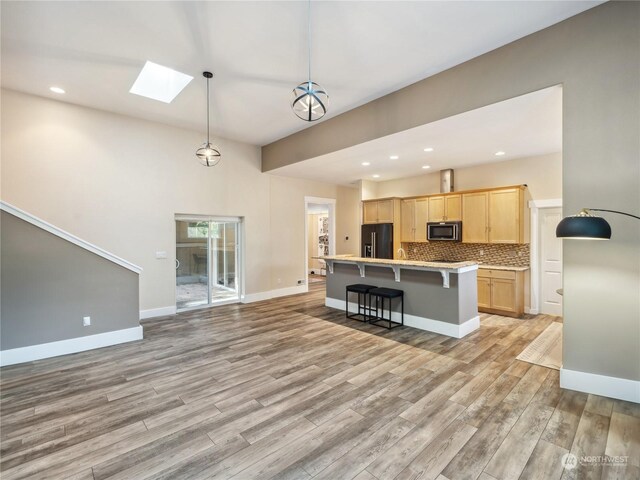 kitchen with a skylight, black refrigerator with ice dispenser, light hardwood / wood-style floors, decorative light fixtures, and light brown cabinetry