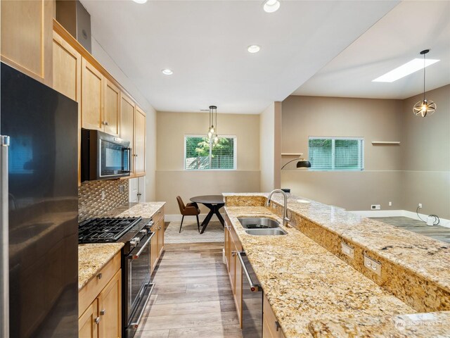 kitchen with light stone counters, stainless steel appliances, sink, light brown cabinets, and hanging light fixtures