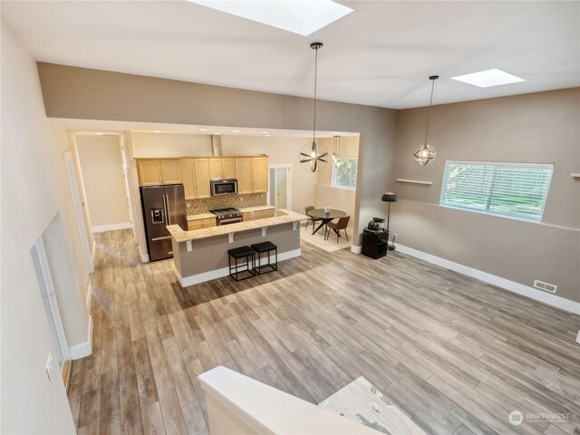 kitchen featuring a kitchen breakfast bar, decorative backsplash, light wood-type flooring, a kitchen island, and stainless steel appliances