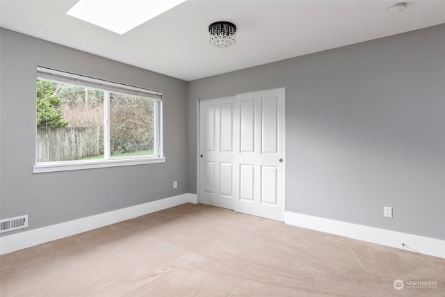 unfurnished bedroom featuring light colored carpet, a skylight, and a closet