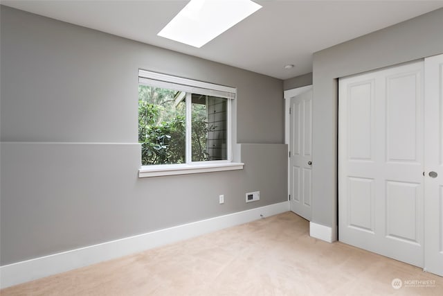 unfurnished bedroom with a skylight, a closet, and light colored carpet