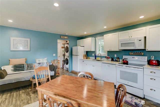 kitchen with white appliances, wood-type flooring, stacked washing maching and dryer, sink, and white cabinets