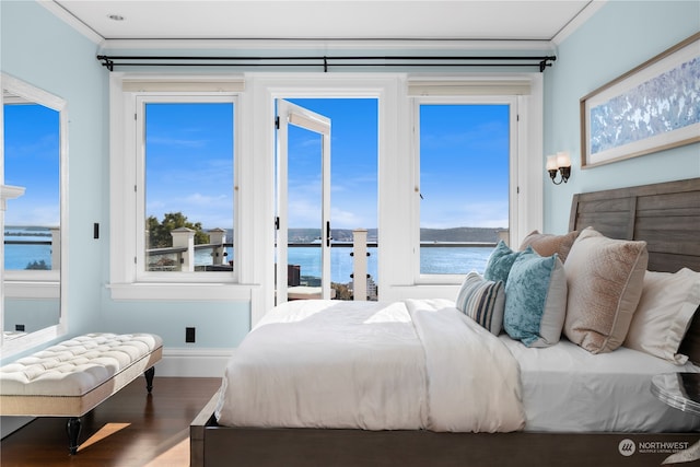 bedroom featuring wood-type flooring, a water view, ornamental molding, and multiple windows