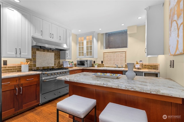 kitchen featuring light stone counters, light hardwood / wood-style floors, tasteful backsplash, a kitchen bar, and appliances with stainless steel finishes