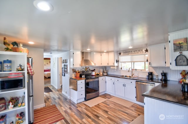 kitchen with white cabinetry, stainless steel appliances, sink, and wall chimney range hood