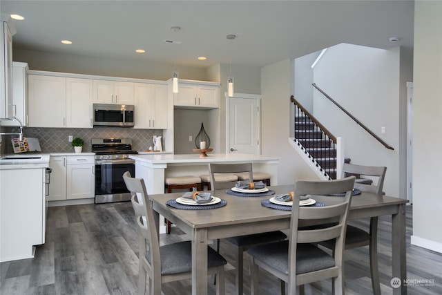 kitchen with appliances with stainless steel finishes, dark wood-type flooring, white cabinets, and hanging light fixtures