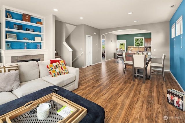 living room with a wealth of natural light, a tiled fireplace, and dark hardwood / wood-style floors