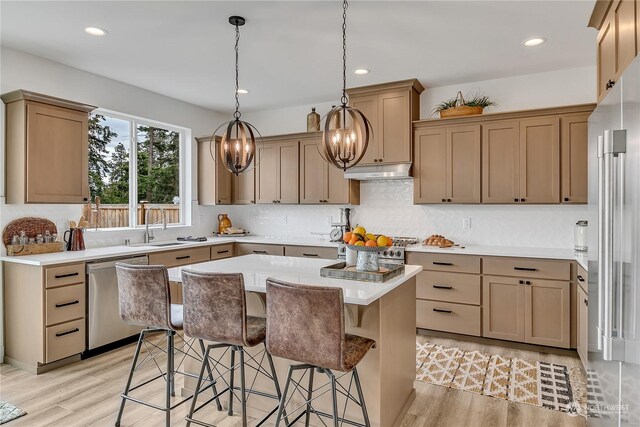 kitchen with pendant lighting, high quality appliances, sink, a center island, and light hardwood / wood-style floors